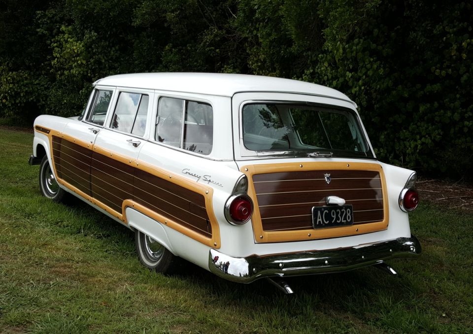 White station wagon with wood paneling, rear passenger side view, parked on grass.