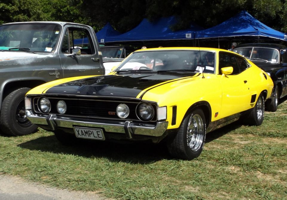 Front view of a yellow and black muscle car parked next to a truck
