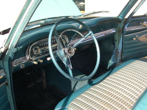 1963 Ford Falcon - The interior of a 1963 Ford Falcon features a teal dashboard, steering wheel, and door panels, complemented by a patterned seat and floor m…