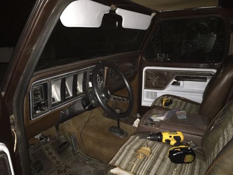 1978 Ford Bronco - The interior of a 1978 Ford Bronco, a brown dashboard, steering wheel, and striped seats with a drill and screws on the passenger seat.