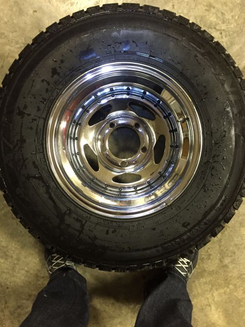 1978 Ford Bronco - A close-up of a shiny chrome wheel and a large tire, with a person's legs and shoes in the frame.
