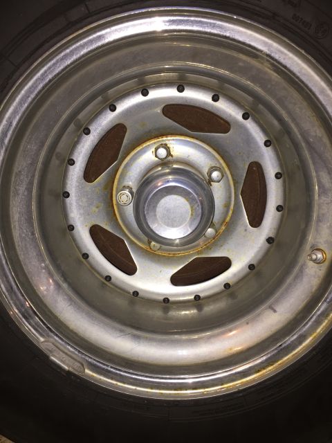 1978 Ford Bronco - Close-up of a chrome wheel with lug nuts and a tire, showing some rust and wear.