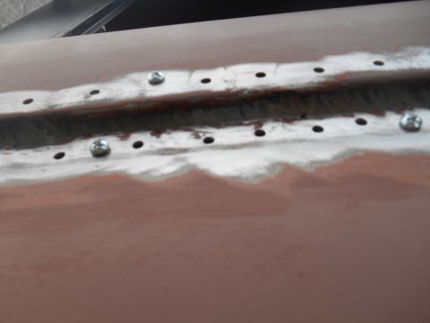 1972 Ford Bronco - Close-up of a car body panel undergoing repair, showing a seam with screws and drilled holes.