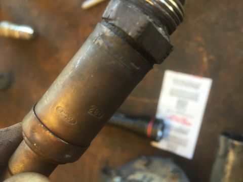 1995 Ford Bronco - A close-up shot shows a brass-colored part with stamped text. Visible markings include an oval Ford logo and the numbers "288".