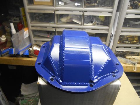1972 Ford Bronco - A bright blue differential cover with visible weld lines is shown in a workshop setting, resting on a cardboard box. The cover is positione…