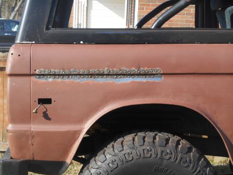 1972 Ford Bronco - A close-up side view of a classic Ford Bronco's rear quarter panel, showing rust repair with visible spot welds along a horizontal seam. Th…
