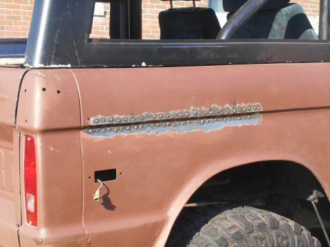 1972 Ford Bronco - A close-up view of the rear quarter panel of a classic Ford Bronco undergoing repair. The panel shows evidence of welding work along a hori…