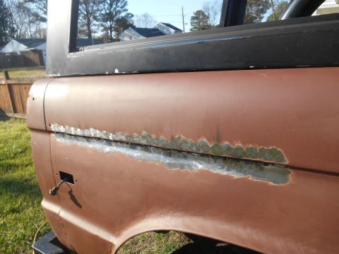 1972 Ford Bronco - Close-up view of the rusted and welded seam on the rear quarter panel of a brown 1972 Ford Bronco. The vehicle is outdoors with grass and a…
