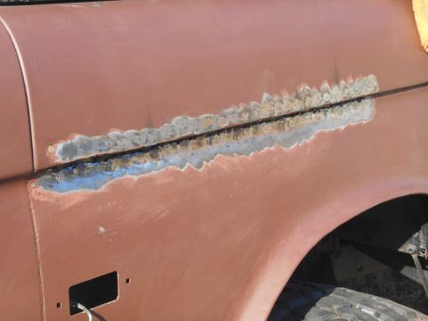 1972 Ford Bronco - Close-up of a rusty seam on a vintage vehicle's body panel, showing areas that have been sanded down to bare metal and possibly prepped for…