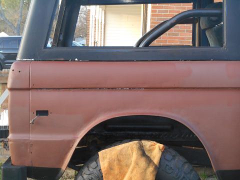 1972 Ford Bronco - Close-up side view of the rear fender and quarter panel of a classic Ford Bronco. The vehicle is painted a reddish-brown primer and has a b…