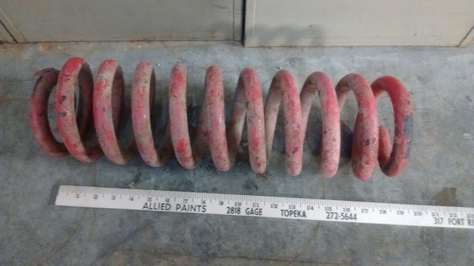 Red coil spring next to a ruler on a concrete floor.