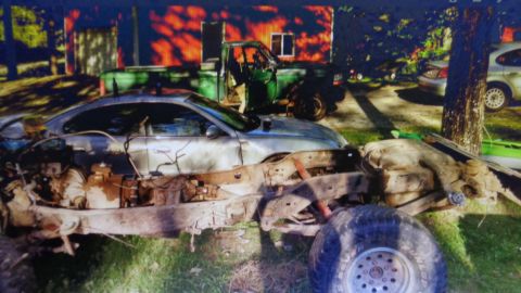 1985 Ford Bronco - A heavily modified car chassis with a silver coupe body is visible in the foreground, with a green pickup truck parked behind it. The scene…