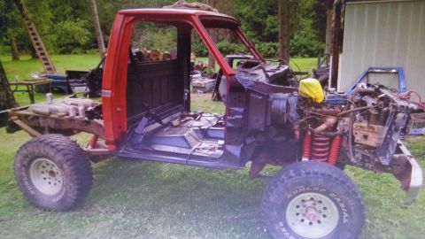 1985 Ford Bronco - A heavily modified red Ford pickup truck cab and chassis sits outdoors on a grassy lawn. The vehicle is in a state of disassembly with the…