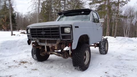 1985 Ford Bronco - A heavily modified, lifted 1980s Ford pickup truck chassis sits in a snowy outdoor setting. The front end is visible, showing a large grill…
