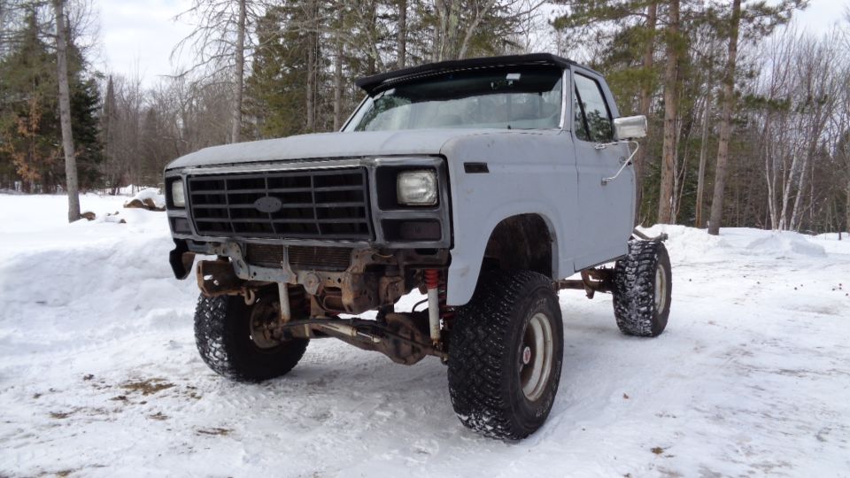 Modified 1980s Ford pickup truck chassis with large tires in the snow.