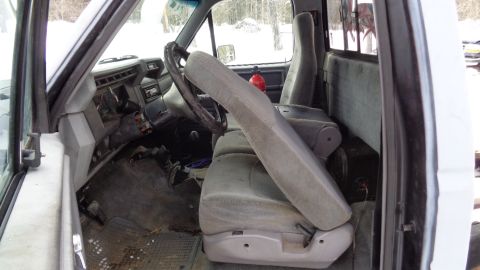 1985 Ford Bronco - The interior of a truck cab is shown, featuring worn grey fabric seats, a dashboard with exposed wiring, and a steering wheel. A red fire e…