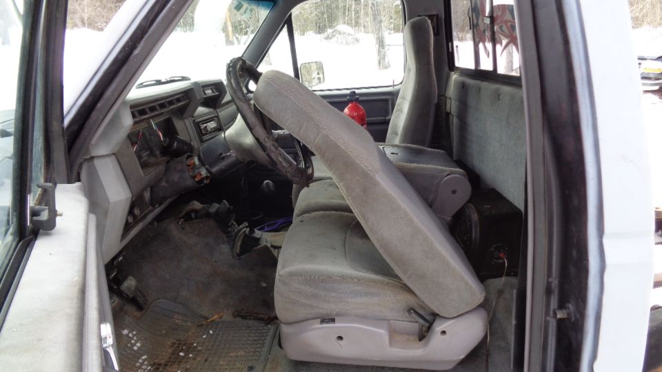 Interior of a truck cab with grey seats, dashboard, steering wheel, and fire extinguisher.