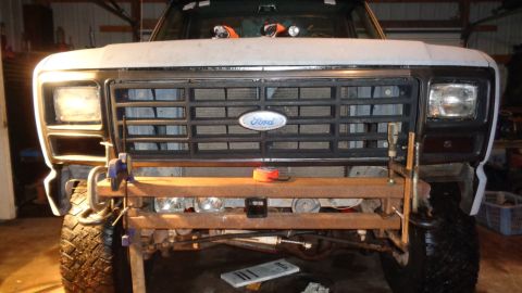 1985 Ford Bronco - The front end of a Ford Bronco is shown, with the grille and headlights visible. A makeshift wooden bumper with clamps is attached to the f…