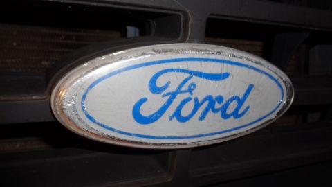 1985 Ford Bronco - A close-up shot of a weathered Ford emblem on the front grille of a vehicle. The oval emblem features the word "Ford" in blue script on a l…