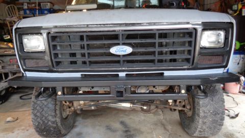 1985 Ford Bronco - Front view of a modified Ford truck with a custom black bumper and a receiver hitch. The vehicle has a gray hood and grille with a Ford emb…