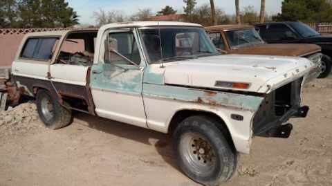 1981 Ford Bronco - A white and teal Ford pickup truck with significant rust and damage is parked outdoors on a dirt lot. The front end is missing, and the pas…