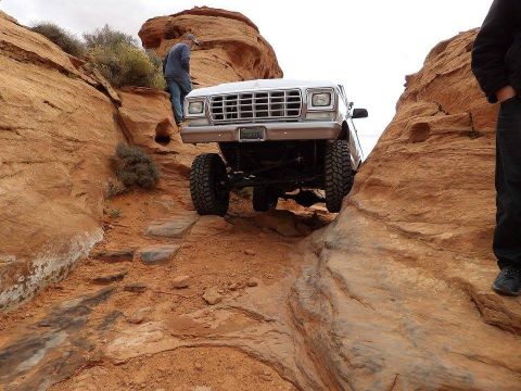 1979 Ford Bronco - A lifted 1979 Ford Bronco is navigating a rocky, off-road trail with a person standing on the side of the path.