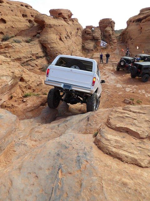 1979 Ford Bronco - A white Ford Bronco is navigating a rocky, off-road trail with steep inclines and large boulders. Several other off-road vehicles are visib…