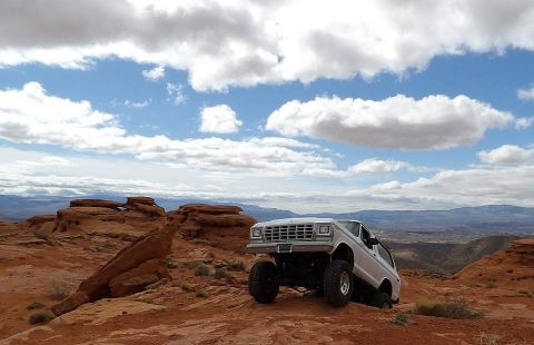 1979 Ford Bronco - A white 1979 Ford Bronco is shown from a 3/4 front angle, parked on a rocky, red-dirt terrain with a vast, hazy landscape in the background…