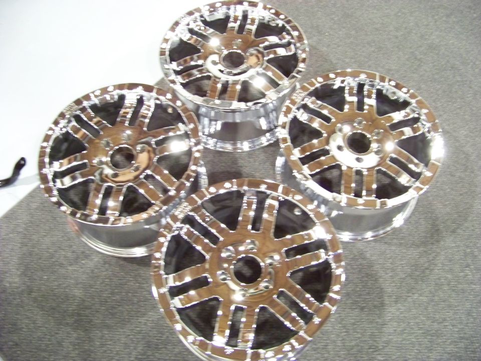 Four chrome aftermarket wheels with a multi-spoke design on a gray carpet.
