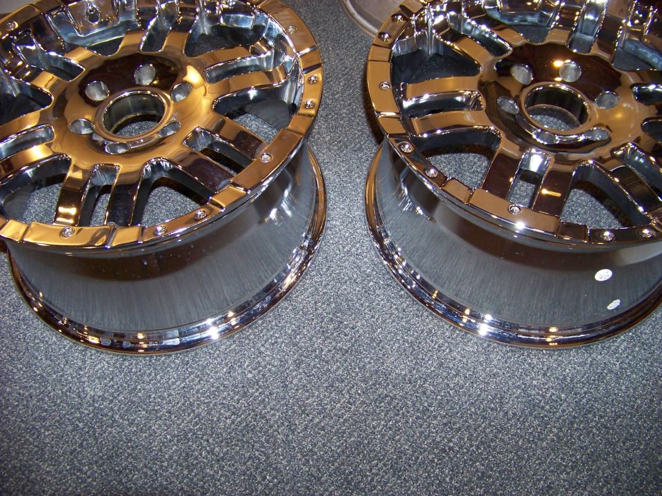 Two shiny chrome aftermarket wheels with multi-spoke design on gray carpet.