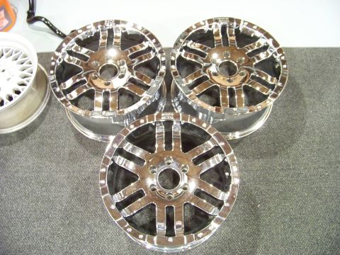 2005 Ford F-150 - Three chrome aftermarket wheels are displayed on a textured gray surface. One wheel is partially visible on the left, and two are stacked i…