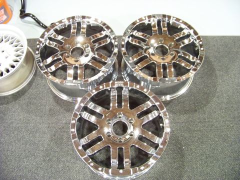 2005 Ford F-150 - Three chrome aftermarket wheels are displayed on a dark gray carpeted surface. One white mesh wheel is visible to the left.