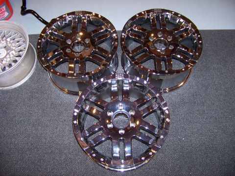 2005 Ford F-150 - Three chrome Moto Metal rims are displayed on a dark gray carpeted surface. One rim is partially visible on the left, and two are fully vis…