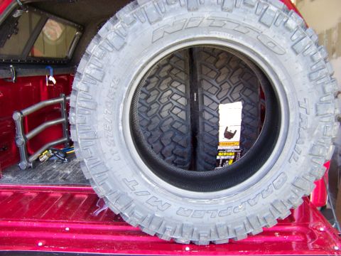 2005 Ford F-150 - A close-up view of two large off-road tires stacked in the bed of a red pickup truck. The tire in the foreground has the text "GRAPPLER M/T…
