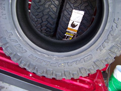 2005 Ford F-150 - A close-up view of a new "Grappler MT" tire, likely for an off-road vehicle, is shown resting on a red surface, possibly the bed of a picku…