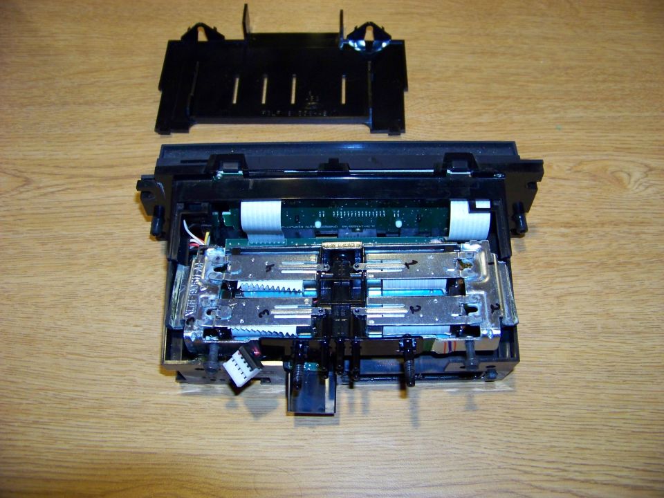 Disassembled electronic component with circuit boards and cables on a wooden surface.