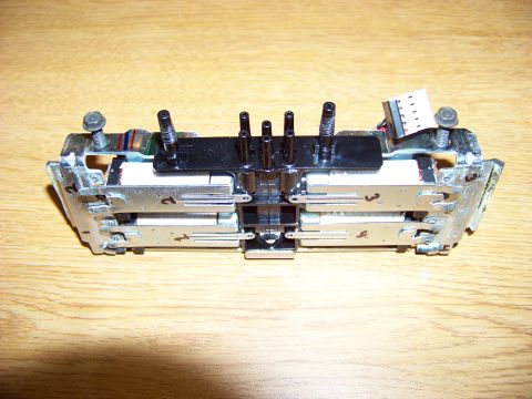 1999 Mercury Grand Marquis - A close-up view of a mechanical assembly with metal and plastic components, screws, and a small electrical connector, set against a wooden…