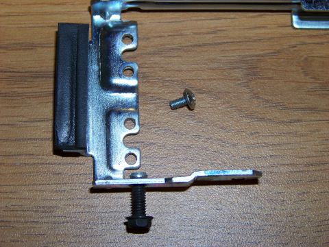 1999 Mercury Grand Marquis - A metal bracket with a rubber insert is shown next to a small screw and a larger bolt with a washer, all resting on a wooden surface.