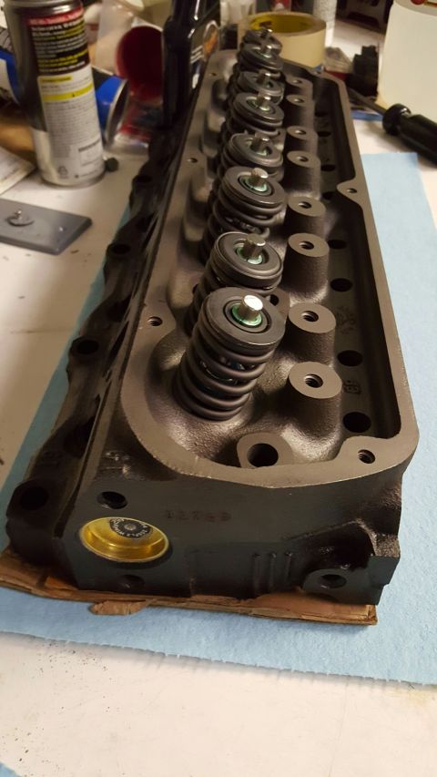 1996 Ford Bronco - A close-up, angled view of a dark gray V8 engine cylinder head with multiple valve springs and retainers visible. The cylinder head is rest…