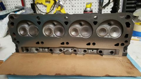 1996 Ford Bronco - A freshly machined cast-iron V8 cylinder head standing deck-side out on a workbench, showing four combustion chambers with newly ground int…