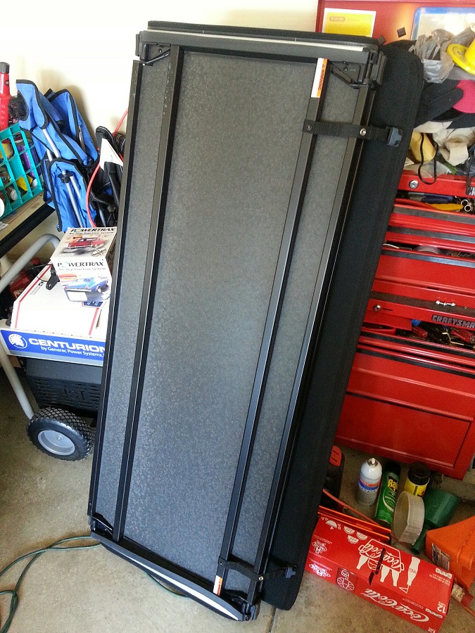 Black tonneau cover leaning against a wall with tools and parts around it.