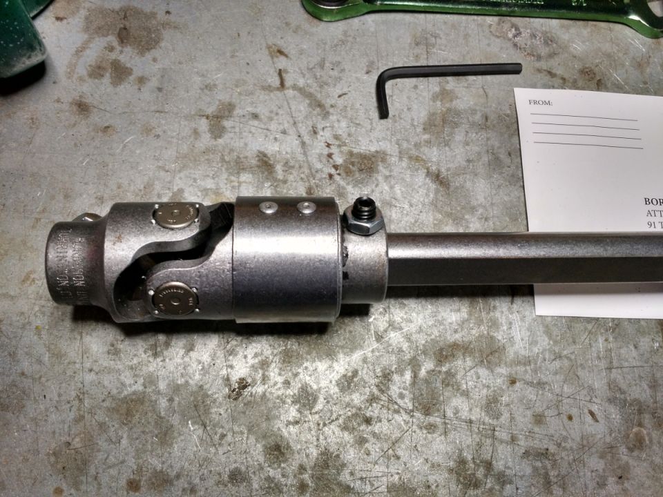 Universal joint assembly on a metal shaft with hex wrench and paper.