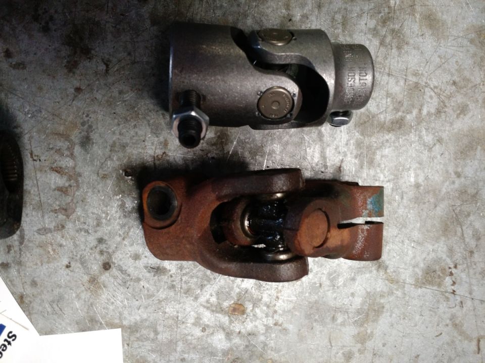 Two steering universal joints, one new and one rusty, on a metal surface