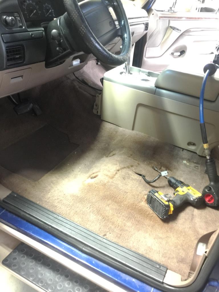 1996 Ford Bronco interior showing tan carpet, dashboard, steering wheel, and center console with tools