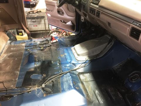 1996 Ford Bronco - The interior of a vehicle is shown with the carpet removed, revealing the floor and wiring beneath.