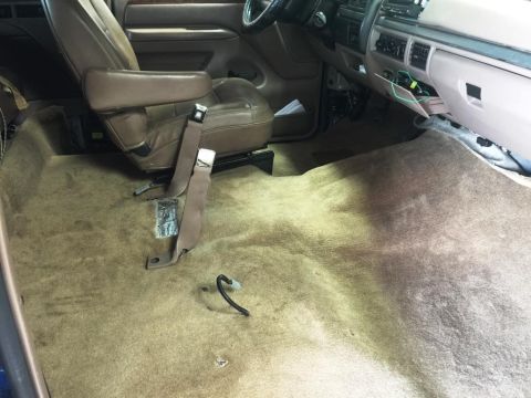 1996 Ford Bronco - The interior of a vehicle shows exposed carpet and a seatbelt, suggesting recent work or disassembly.