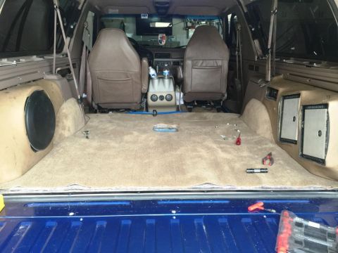 1996 Ford Bronco - The interior of a 1996 Ford Bronco shows tan carpeting and brown seats, with a blue tailgate visible at the rear.