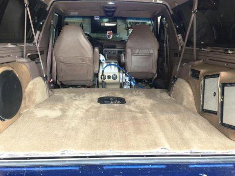 1996 Ford Bronco - The interior of a 1996 Ford Bronco features tan carpeting, bucket seats, and custom speaker enclosures.