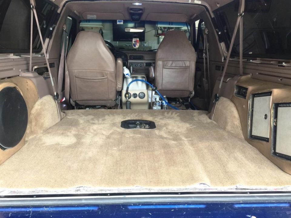 Interior of a 1996 Ford Bronco showing tan carpet, seats, and custom speaker boxes