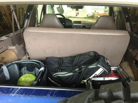 1996 Ford Bronco - The interior of a vehicle's cargo area is filled with sports equipment and bags, in the foreground, a blue surface.